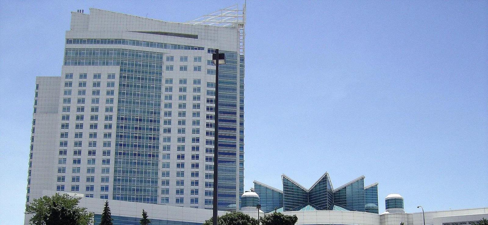 The hotel tower and fan-shaped glass atrium of Caesars Windsor rising above the trees — Caesars Windsor