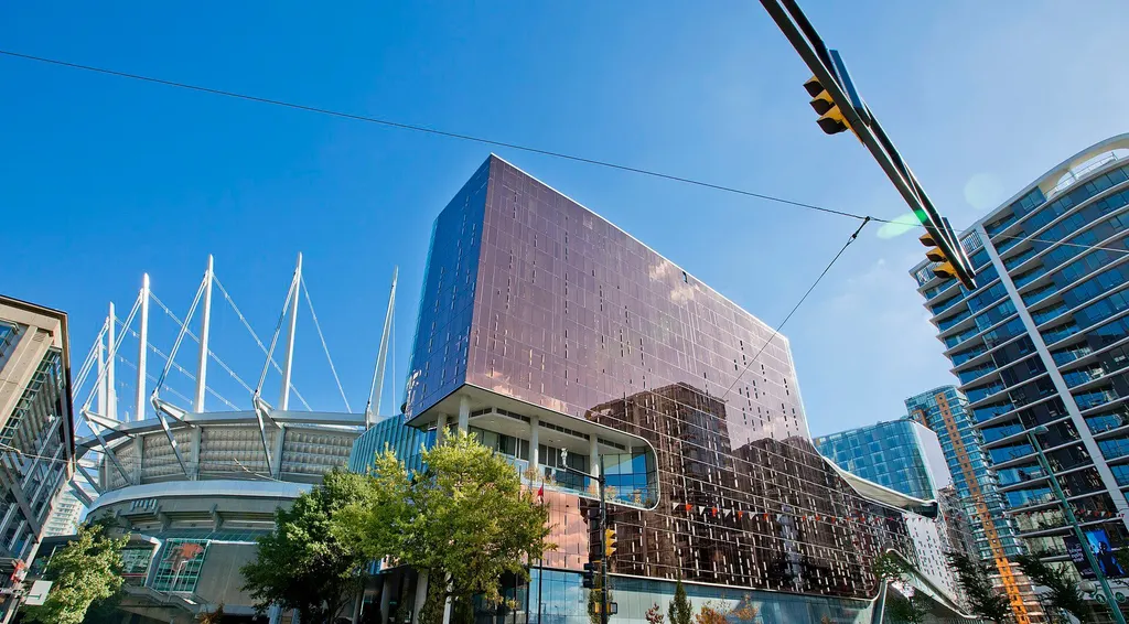 Parq Vancouver's glass tower beside the roof masts of BC Place stadium, seen from street level. — Parq Casino